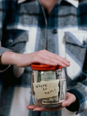 Woman in plaid shirt holds money jar with travel goals in mind.