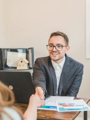 pexels photo 8293749 8293749 A professional real estate agent welcomes a client in the office with documents on the desk.