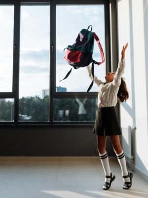 pexels photo 8926553 8926553 A joyful girl in school uniform tossing her backpack in a sunlit classroom.
